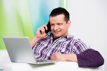 attraktiver mann telefoniert und schaut aufs laptop