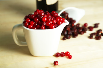 Fresh and dry cranberry in pitchers on wooden table close-up