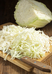 Chopped cabbage strips on a cutting board and a head of cabbage. © severga