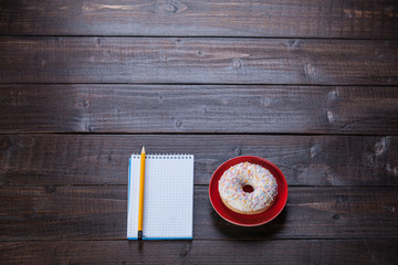 Notebook, donut and pencil on wooden table.