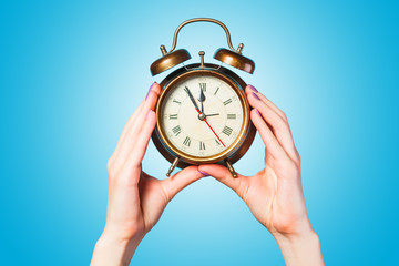 Hands holding alarm clock on blue background.