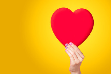 Hands holding shape heart on yellow background.