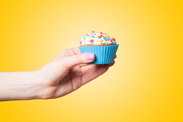 Hand holding cupcake on yellow background