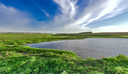 Lake and green summer meadow  with blue cloudy sky in  windy day