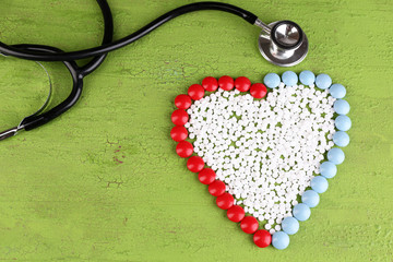 Heart of pills and stethoscope on wooden background
