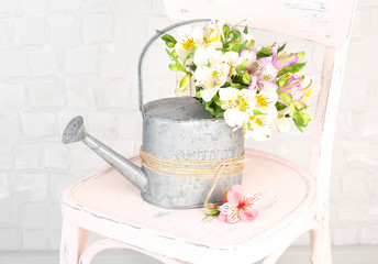 Beautiful bouquet of freesias in watering can on chair in room