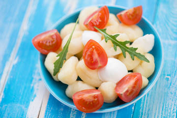 Boiled gnocchi with mozzarella, tomatoes and arugula lettuce