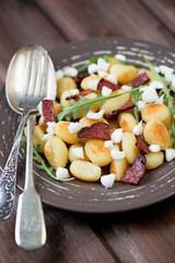 Roasted gnocchi with cheese, meat and arugula in a glass plate