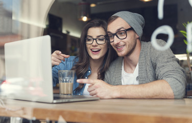 Couple have fun while looking on laptop at cafe