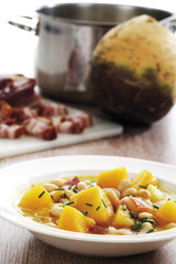Steckrübe Gemüsesuppe mit Bohnen und Speck, Steckrüben Korm , Speck und Topf im Hintergrund