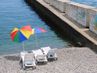 Белые шезлонги с разноцветными зонтиками на пляже Алушты в Крыму.
