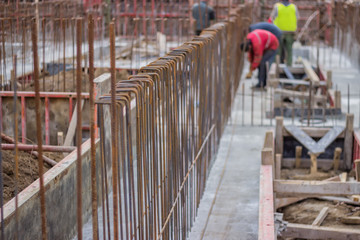 Naklejka premium Blurred workers and steel reinforcement in foundation of new bu