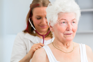 Doktor bei Atmung abhören von Seniorin in Arztpraxis