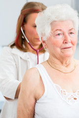 Doktor bei Atmung abhören von Seniorin in Arztpraxis