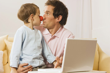 Vater und Sohn ( 4-5) am Laptop,Junge trägt Clown-Nase