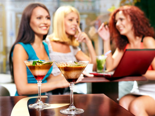 Women at laptop drinking cocktail in a cafe.Sharpness on glasses