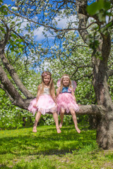 Little adorable girls sitting on blossoming apple tree