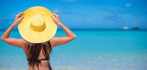 Woman sitting in yellow hat on white sand beach enjoying summer