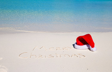 Santa Hat on white sandy beach and Merry Christmas written in