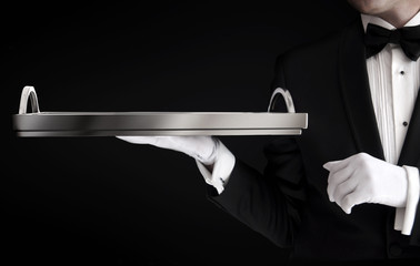 Waiter in tuxedo holding an empty tray isolated on black