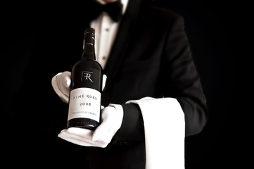 Waiter in tuxedo holding a bottel of red wine