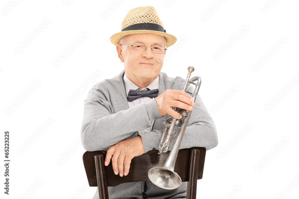 Wall mural Senior gentleman holding trumpet seated on chair