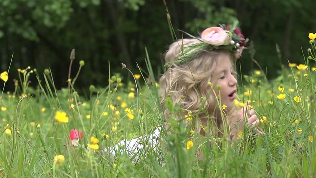 Cute little blond girl poses lying in the grass