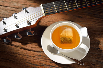 Cup of tea with tea bag and guitar on wooden table