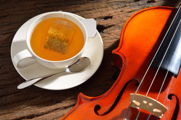 Cup of tea with tea bag and violin on wooden table