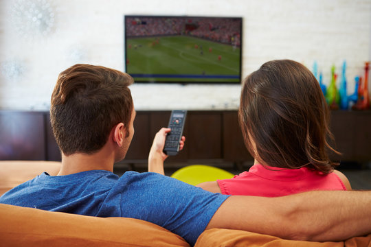 Rear View Of Couple Sitting On Sofa Watching TV Together