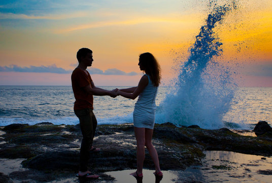 young couple standing hand in hand on shore in evening at sunset