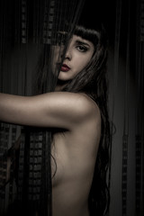 Elegant naked woman behind a curtain of black threads