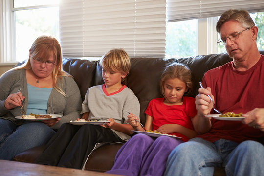 Family With Poor Diet Sitting On Sofa Eating Meal