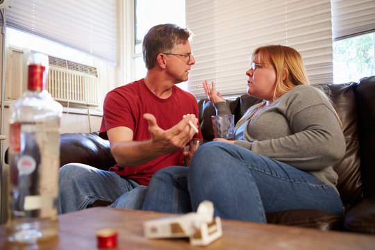 Couple Arguing On Sofa With Bottle Of Vodka And Cigarettes