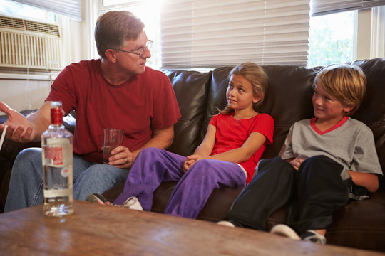 Father Sits On Sofa With Children Smoking And Drinking