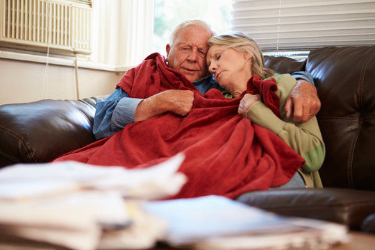 Senior Couple Trying To Keep Warm Under Blanket At Home