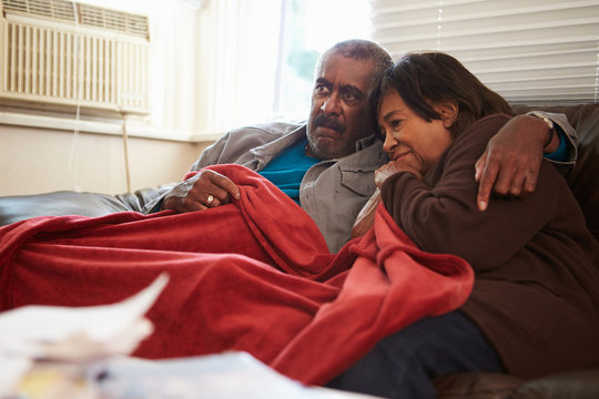 Senior Couple Trying To Keep Warm Under Blanket At Home