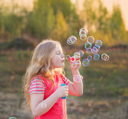 girl blowing soap bubbles outdoor at sunset