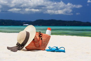hat, bag, sun glasses and flip flops on tropical beach