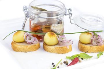 pickled herring in a glass jar with potato canapes