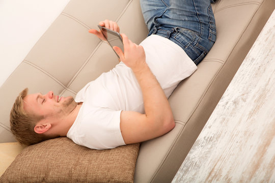 Junger Mann mit dem Tablet PC auf dem Sofa