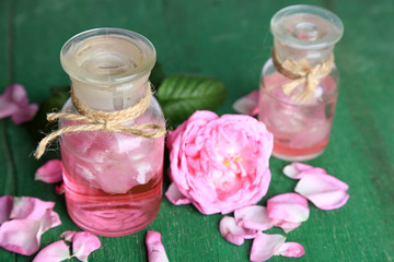 Rose oil in bottles on color wooden background