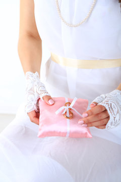 Bride in white dress and gloves holding decorative pillow with