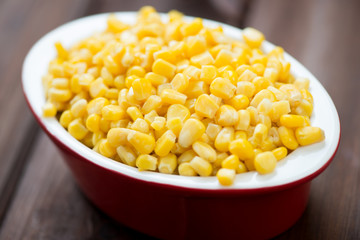 Glass bowl with corn kernels, wooden background, studio shot