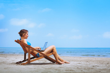 woman in bikini sitting with laptop on the beach