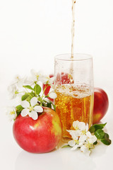 Glass of fresh apple juice with ripe red apples and blooming flo