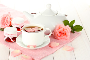 teapot and cup of tea with roses and jam on white wooden table