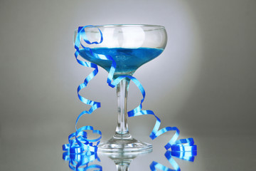 Glass of cocktail and streamer after party on gray background