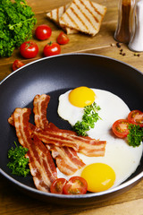 Scrambled eggs and bacon on frying pan on table close-up