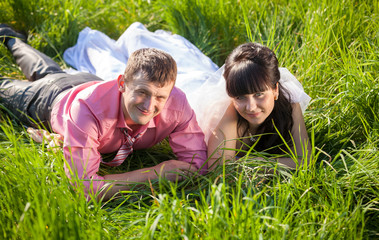 Naklejka na ściany i meble smiling bride and groom lying on field at summer